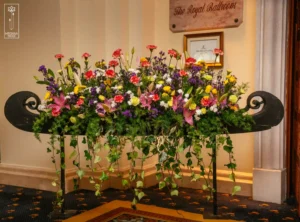 Decorative floral arrangement with colorful flowers and hanging greenery on a black stand.